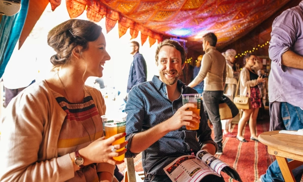 A woman and a man smile and enjoy drinks in a vibrant, colorful indoor setting with patterned decorations and a lively atmosphere.