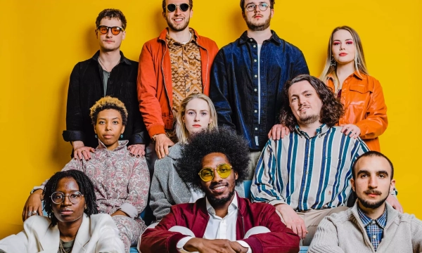 A diverse group of ten people posing together in front of a bright yellow background, showcasing various styles and expressions.