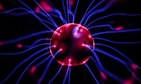 A close-up of a plasma ball with vibrant purple and red electric arcs extending from a central globe, creating a dynamic and colorful display of energy.