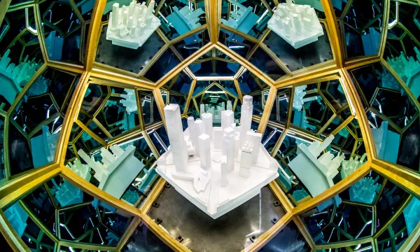 A mirror installation featuring a variety of white architectural models arranged on a central platform, surrounded by kaleidoscopic reflections.