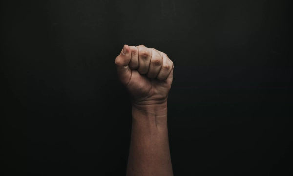 A raised fist against a dark background, symbolizing resistance, solidarity, or empowerment.