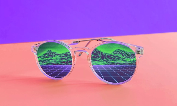 A pair of round, transparent sunglasses with vibrant green and purple geometric patterns reflected in the lenses, set against a two-toned purple and orange background.