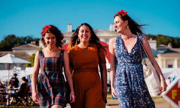 Three young women walking together, smiling and enjoying a sunny day, wearing stylish outfits and flower hair accessories.