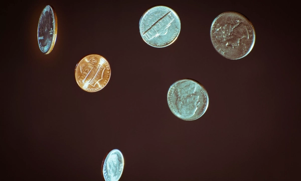 A collection of various coins, including a penny and several quarters, floating against a dark background.