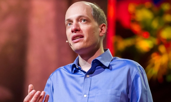 A man wearing a blue shirt speaks passionately on stage, gesturing with one hand, during a TED Talk.