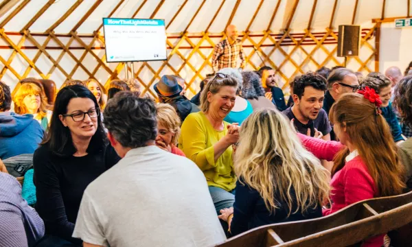 A group of people engaged in conversation in a warm, cozy setting with a wooden interior, showcasing a vibrant community atmosphere.