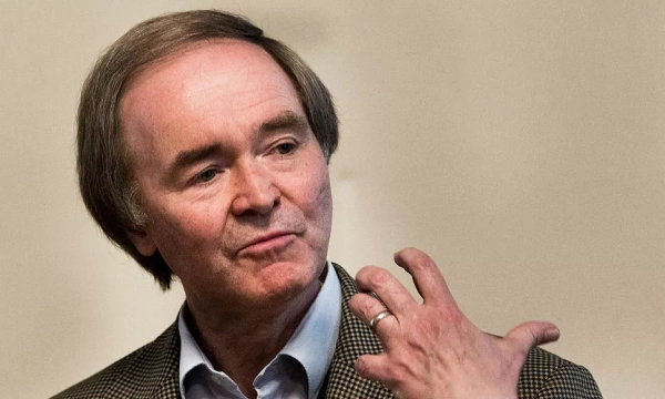 A man with short hair wearing a checkered jacket gestures with his hand while speaking, likely engaged in a discussion or presentation.