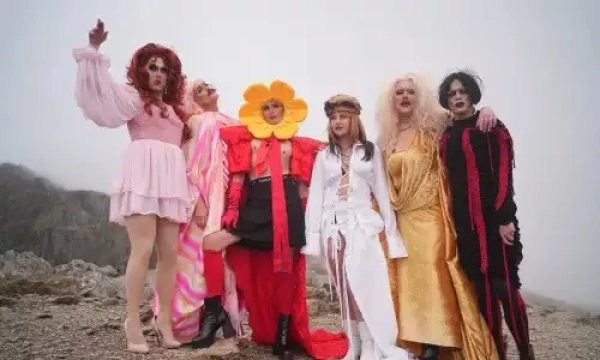 A group of six individuals dressed in colorful and extravagant outfits, posing dramatically outdoors on a foggy day.