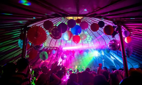 Colorful disco tent filled with partygoers dancing under vibrant lights and decorations, creating a festive atmosphere.