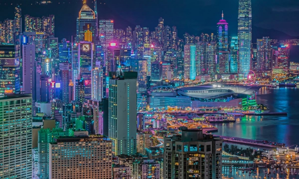 A stunning nighttime view of Hong Kong's skyline, featuring brightly lit skyscrapers and vibrant colors reflecting on Victoria Harbour.