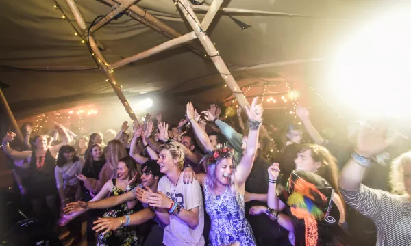 A lively crowd at a music festival, enjoying the performance, dancing, and celebrating under soft lights in a tent-like setting.