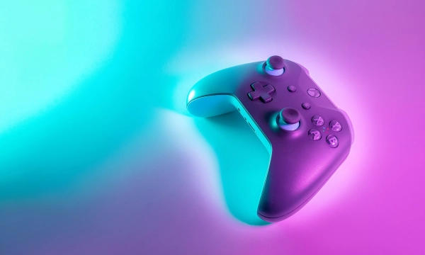 A purple and teal illuminated gaming controller positioned on a light background, showcasing a modern design and ergonomic shape.