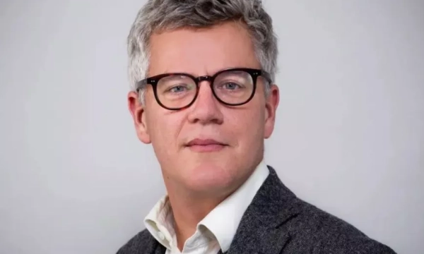 A middle-aged man with glasses and gray hair, wearing a suit jacket over a white shirt, looking directly at the camera against a light background.