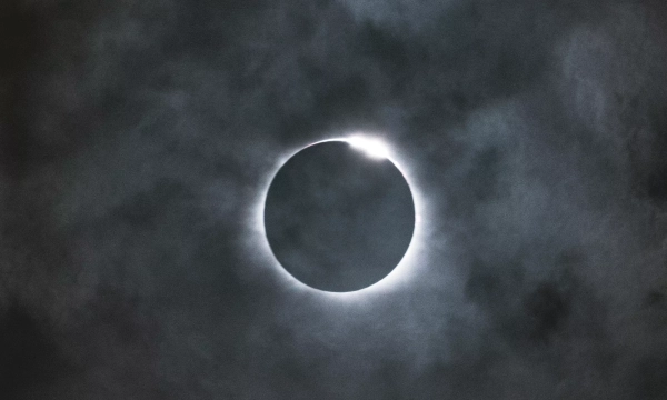 A darkened sky during a solar eclipse, showcasing a ring of light surrounding the moon as it partially obscures the sun.