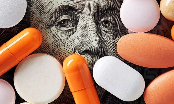 Pills and capsules of various colors scattered over a background featuring a close-up of Benjamin Franklin's face on a dollar bill.