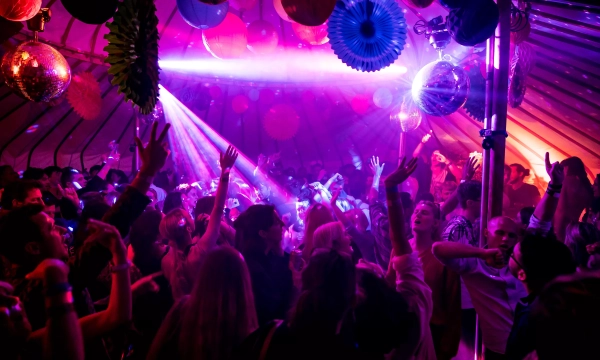 A vibrant dance party scene with a lively crowd raising their hands under colorful lights and disco balls, creating an energetic atmosphere.