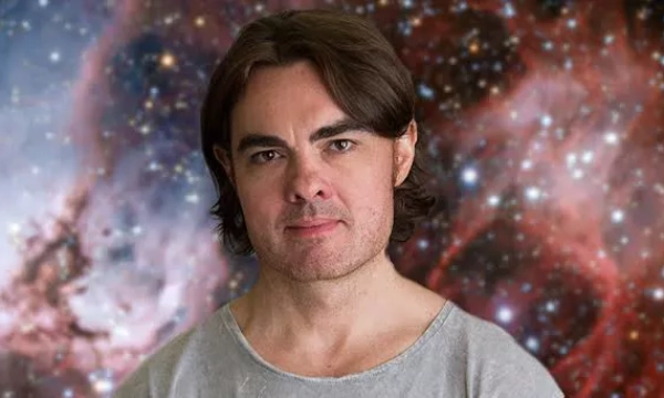 A man with long dark hair poses against a colorful cosmic background filled with stars and nebulae.