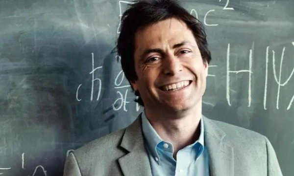 A smiling man in a suit stands in front of a chalkboard filled with mathematical equations and symbols.