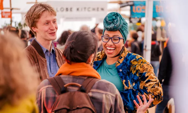 A diverse group of people engaged in a lively conversation, smiling and expressing joy at a communal event indoors.