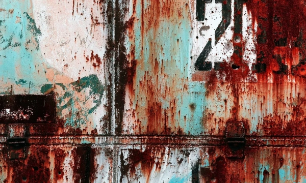 A weathered and rusted surface with splashes of red and blue paint, featuring a partially obscured number "21" and hints of abstract figures.