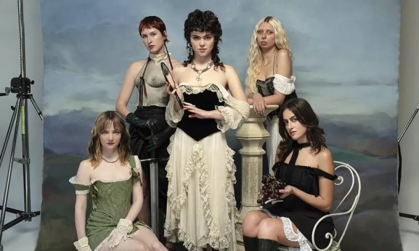 A group of five women poses in front of a scenic backdrop, wearing a mix of vintage and contemporary outfits, showcasing diverse styles and expressions.
