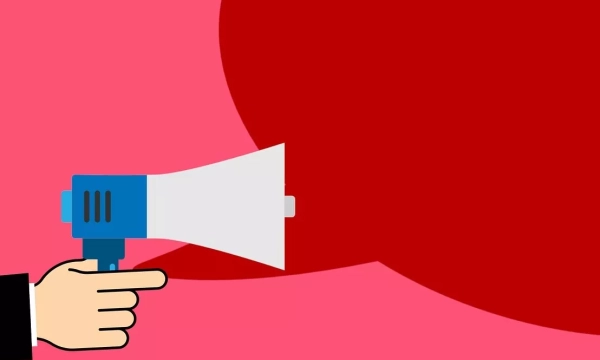 A graphic of a hand holding a blue megaphone on a pink background, with a large red speech bubble suggesting communication or announcement.