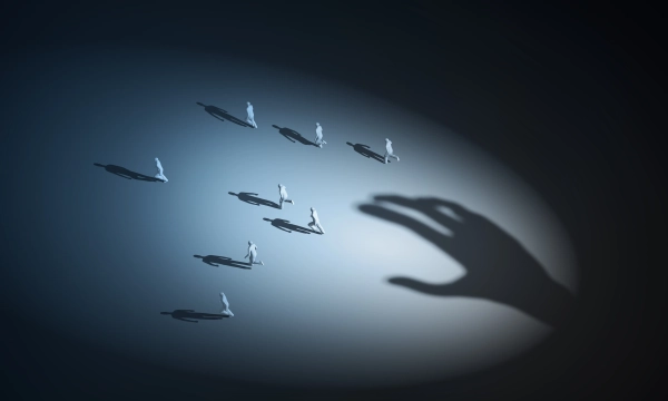 A large hand shadow reaches towards small, scattered white figures, creating a dramatic interplay of light and shadow in a surreal, abstract setting.