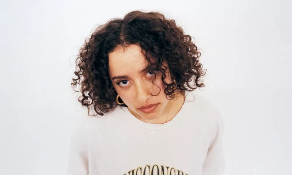 Young person with curly hair wearing a Wisconsin-themed t-shirt, looking directly at the camera against a plain white background.