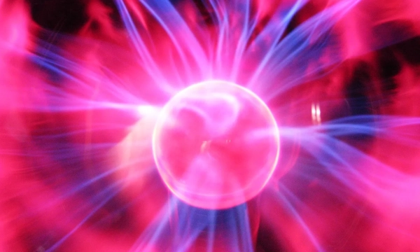 A colorful display of electric plasma swirling around a central glowing orb, showcasing vibrant pink and blue hues in a dynamic light pattern.