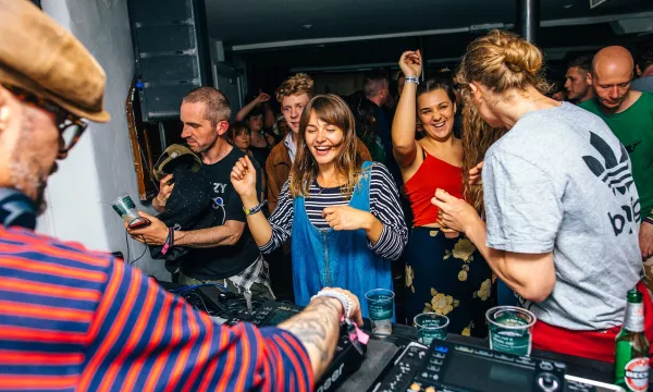 A lively party scene with people dancing, enjoying music from a DJ, in a vibrant atmosphere filled with energy and smiles.